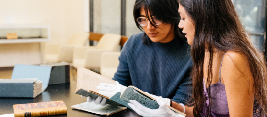 two students sitting at desk review rare book materials